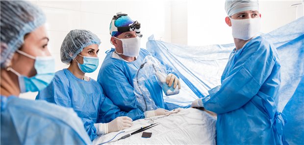 Brustkrebs: Bilaterale Mastektomie wirkte risikoreduzierend auf die Gesamtmortalität Ein Team von Chirurgen ist über eine Frau am Op-Tisch gebeugt.