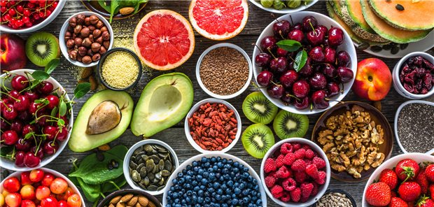 Auswahl an gesunden pflanzlichen Lebensmitteln: Superfoods, verschiedene Obstsorten und Beeren, Nüsse und Samen.