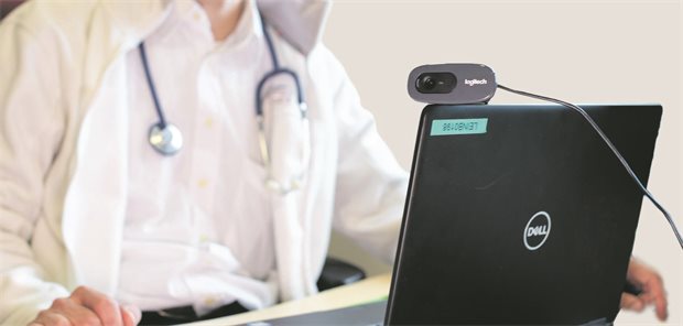 Arzt sitzt vor Laptop mit aufmontierter Kamera