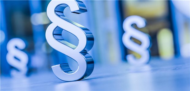 Ein Paragrafenzeichen in blau und im Hintergrund verschwommene Paragrafen.