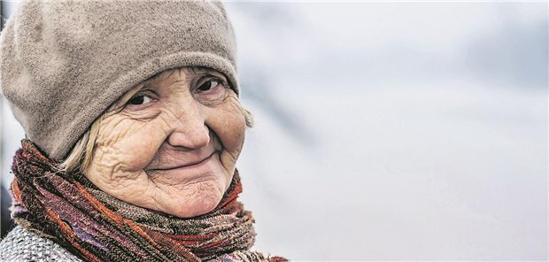 Eine alte Dame schaut lächelnd in die Kamera. Sie hat eine Mütze und einen Schal an.