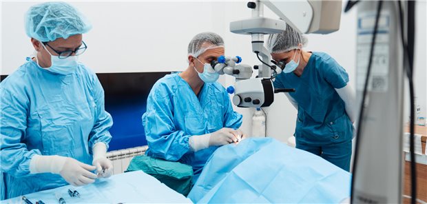 Ein Ärzte im OP über einen mit einem Tuch abgedeckten Patienten während einer Operation am Auge.