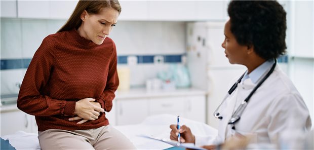 Erwachsene Frau legt sich wegen Unterleibsschmerzen die Hände auf ihren Bauch bei einem Arzttermin.