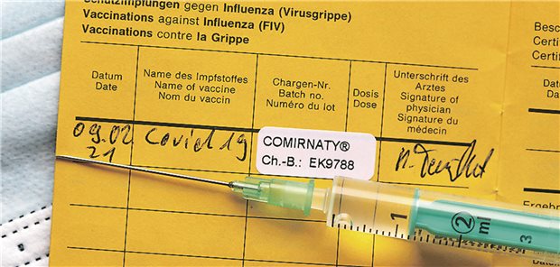 Aufgeschlagener Impfpass mit Impfspritze und einem Aufkleber, der die COVID-19-Impfung mit Comirnaty® dokumentiert.