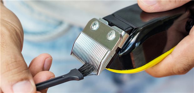 Eine Person reinigt mit einer Bürste eine elektrische Haarschneidemaschine.