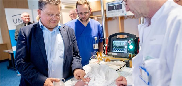 Andreas Philippi (SPD), Gesundheitsminister in Niedersachsen, Chris Mohrmann, Facharzt für Anästhesiologie an der Universitätsklinik für Kinder- und Jugendmedizin, und Axel Heep, Direktor der Universitätsklinik für Kinder- und Jugendmedizin am Klinikum Oldenburg (v.l.n.r.), demonstrieren die Reanimation eines Säuglings anhand einer Puppe, während im Hintergrund ein Patientenmonitor mit telemedizinischer Verbindung zu erkennen ist.