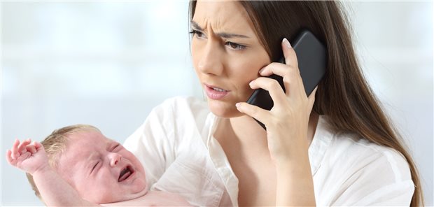 Bei Kassen-Bescheid am Telefon: Sofort reagieren! Junge Frau mit Säugling im Arm am Telefon, das Gesicht zweifelnd und verärgert verzogen.