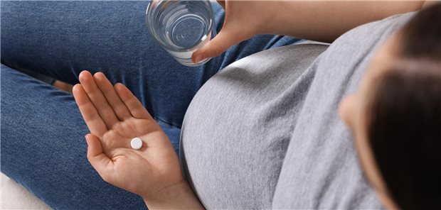 Eine schwangere Frau hält eine Tablette in der einen Hand und in der anderen Hand ein Glas Wasser.