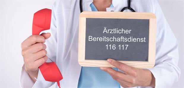 Arzt hält rotes Telefon in der Hand und in der andren ein Schild mit der Aufschrift „Ärztlicher Bereitschaftsdienst 116 117“.