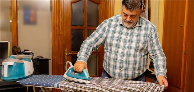 Ein übergewichtiger Mann bügelt ein Hemd.