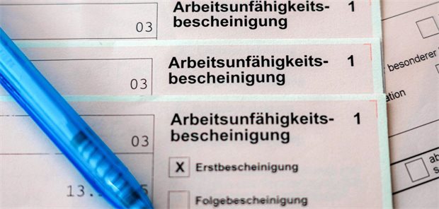  Mehrere Exemplare einer Arbeitsunfähigkeitsbescheinigung liegen übereinander, daneben ein Kugelschreiber. 