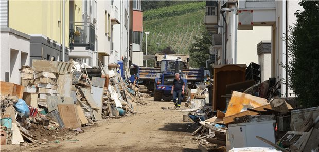 Kammern bitten um Geldspenden für flutgeschädigte Ärzte Bad Neuenahr: Straße, in der sich der Schutt etwa mannshoch türmt; Es wird allerdings schon aufgeräumt - ein Fahrzeug mit Frontlader fährt Schutt in einen Hänger.