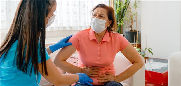 Frau fasst sich an den Bauch und blickt schmerzerfüllt zu einer Ärztin (Symbolbild mit Fotomodellen).