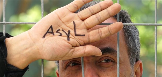 Mensch hinter einem Zaun mit der Aufschrift &quot;Asyl&quot; auf seiner Hand.