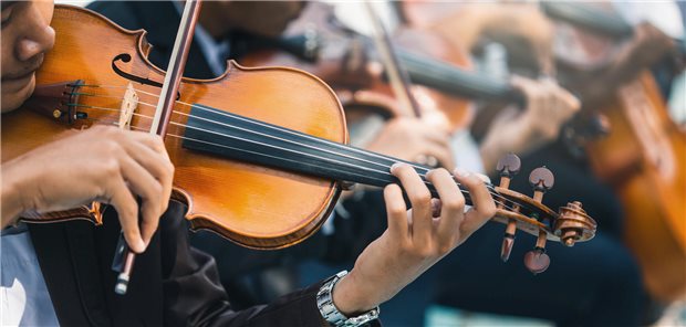 Wenn Musikmachen Muskeln, Sehnen und Gelenke krank macht Nahaufnahme eines männlichen Geigers, der als Teil eines Sinfonieorchester klassische Musik spielt.