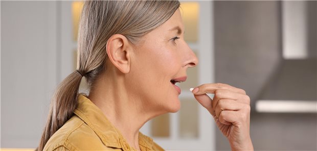 Eine Frau nimmt im Rahmen ihrer postmenopausalen Hormonersatztherapie in der Küche eine Tablette ein.