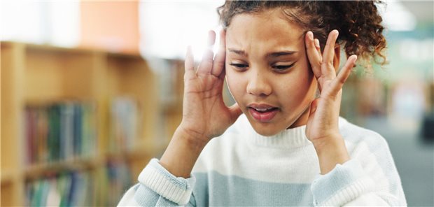 Ein junges Mädchen halt sich den schmerzenden Kopf fest. 