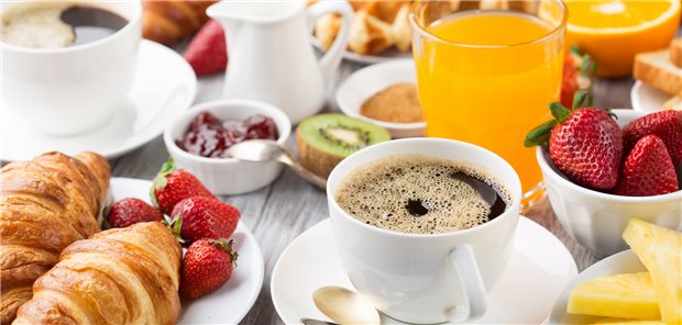 Voller Frühstückstisch mit Kaffee, Orangensaft, Orangen, Erdbeeren, Kiwi und Croissants