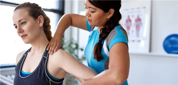 Junge Frau wird von einer Physiotherapeutin an der Schulter behandelt.