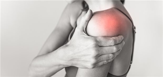 Eine Frau hält sich mit der rechten Hand die linke Schulter, die schmerzt.