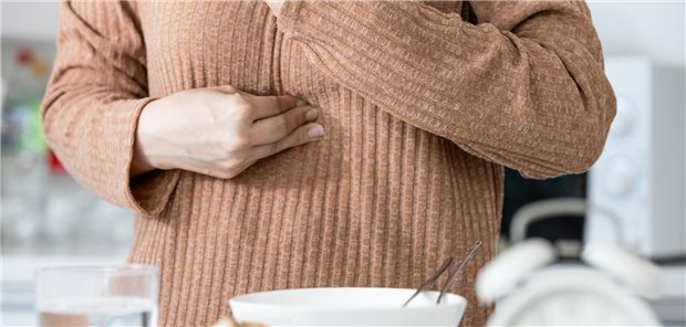 Eine Frau greift sich mit beiden Händen auf die Brust. Vor ihr steht eine Schüssel mit Essen. 