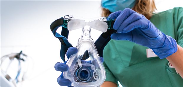 Eine Pflegerin setzt einem Patienten eine Atemmaske auf.