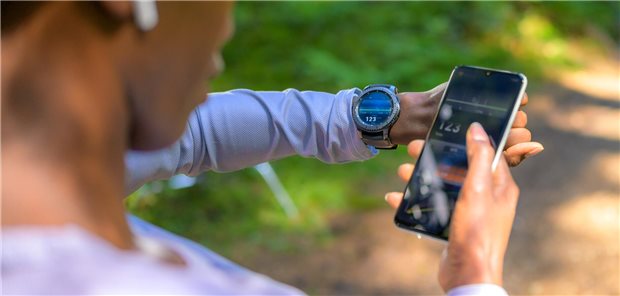 Ein Mann schaut auf seine Smartwatch und auf sein Smartphone
