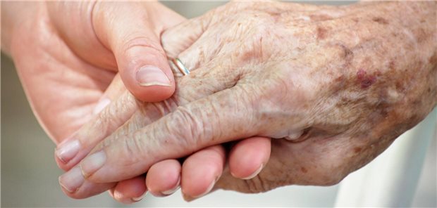 Was bei einem palliativmedizinischen Notfall Priorität hat Eine Frau hält ihrem bettlägerigen Mann die Hand.