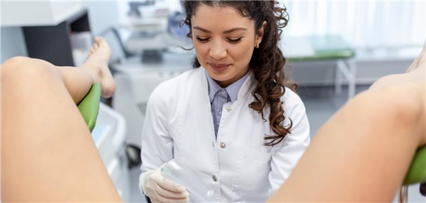 Eine Gynäkologin, die ein Vaginalspekulum zur Untersuchung einer Patientin, die auf einem gynäkologischen Stuhl liegt, in der Hand hält.