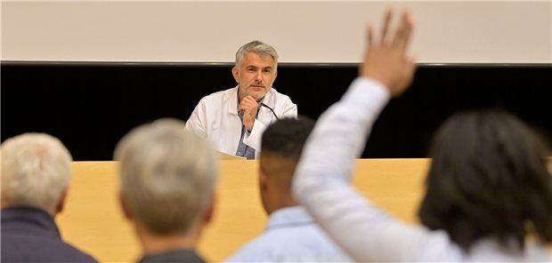 Ein Arzt hält einen Vortrag in einem Kongresszentrum mit Publikum im Hintergrund.