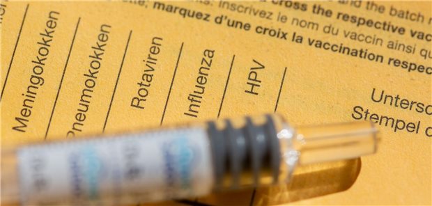 Eine Spritze liegt auf einem Impfpass, in dem verschiedene Schutzimpfungen, wie gegen Meningokokken, aufgeführt sind.