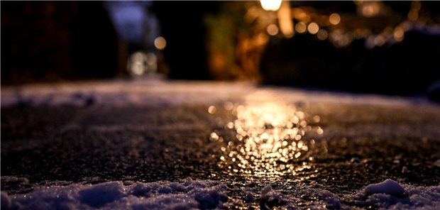 Ein vereister Gehweg glitzert im Schein einer Laterne.