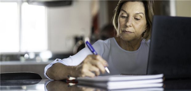 Frau schreibt in der Küche und hat einen Laptop vor sich stehen.
