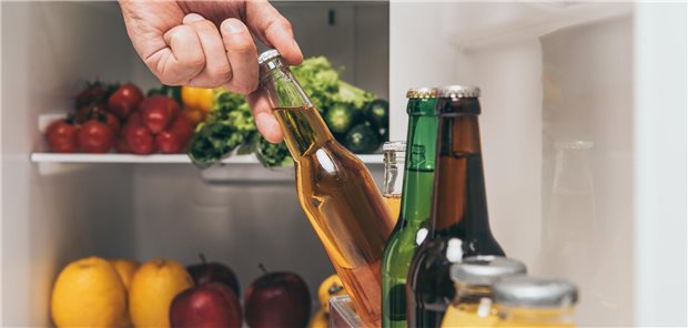 Eine Person greift eine Flasche Bier aus einem gefüllten Kühlschrank.