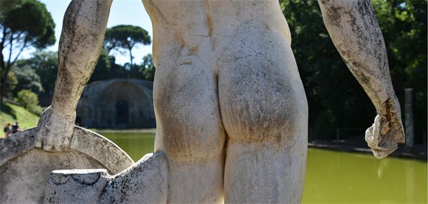 Römische Statue von hinten in einer Gartenanlage.