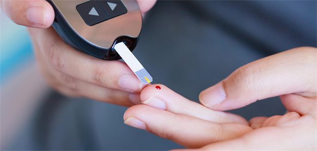 Ein Mensch misst seinen Blutzucker und sticht sich in einen Finger.