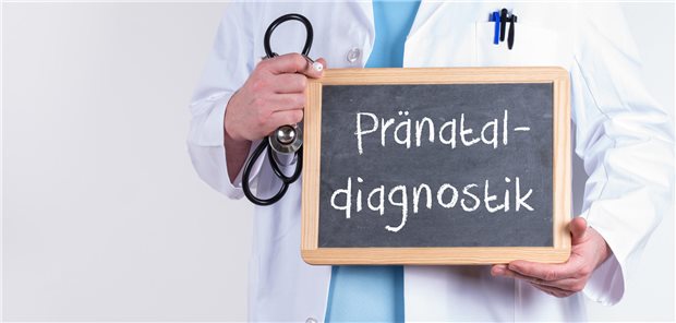 Das Foto zeigt eine Tafel mit der Aufschrift "Pränatal-Diagnostik", die von einer Person mit Stethoskop in der Hand gehalten wird.