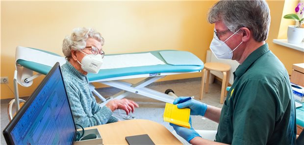 Neue STIKO-Empfehlungen zu COVID-19-Impfung für Genesene Patientin sitzt beim Arzt, der etwas ins Impfbuch einträgt.