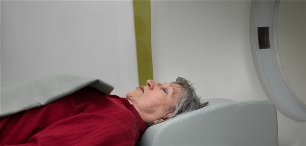 Symbolbild: Dame mit grauem Haar liegt mit geschlossenen Augen am Eingang eines CTs: Bei COVID und akuter Enzephalopathie ist die Prognose schlecht.
