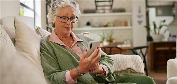 Eine ältere Dame sitzt auf einem Sofa und schaut auf ihr Handy.