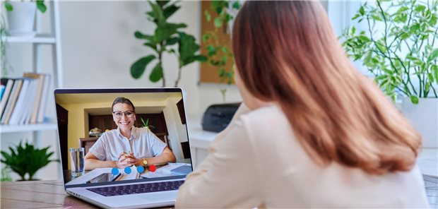 Eine junge Frau bei einer Online-Therapie mit einer Psychologin/Psychotherapeutin, unter Verwendung einer Videokonferenz auf einem Laptop.