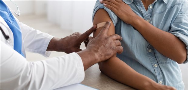 Ein Arzt klebt einer schwangeren Frau ein Pflaster auf den Oberarm.