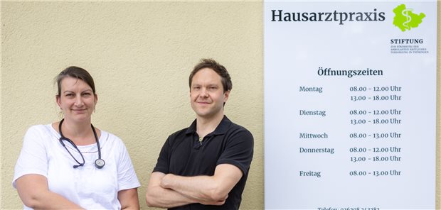 Dagmar Heuer und Dr. Bastian Morgenroth neben dem Praxisschild.
