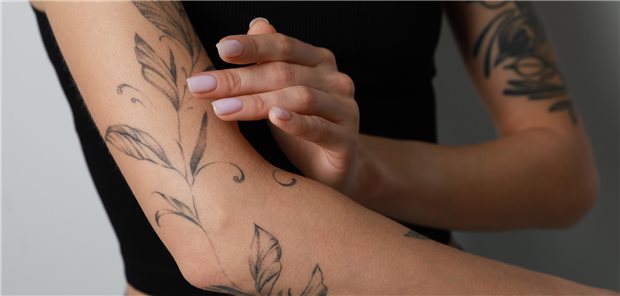 Eine Frau streicht sich mit der Hand über den rechten Arm, auf dem sich die Tätowierung einer Kletterpflanze befindet.