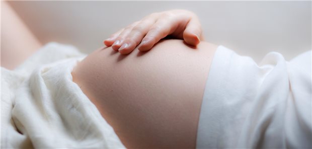 Eine schwangere Frau liegt auf dem Rücken und hat ihre rechte Hand auf dem Bauch.