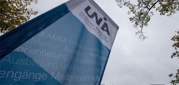 Vor dem Lehrgebäude der medizinischen Fakultät der Universität Augsburg steht ein Banner mit dem Logo und dem Schriftzug der Fakultät.