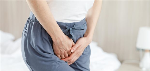 Eine Frau hat Schmerzen im Unterbauch aufgrund einer Blasenentzündung und hält sich mit der Hand den unteren Bauch.