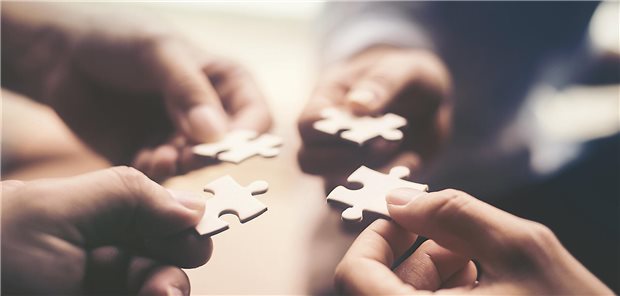 Vier Hände halten Puzzle-Teile zusammen.