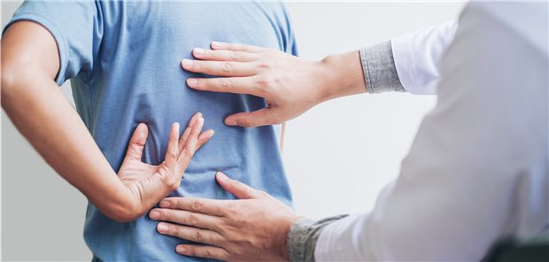 Rückenschmerzen: Forschungsgruppe sagt Therapieversagern den Kampf an Arzt fasst einem Patienten behutsam an den schmerzenden Rücken