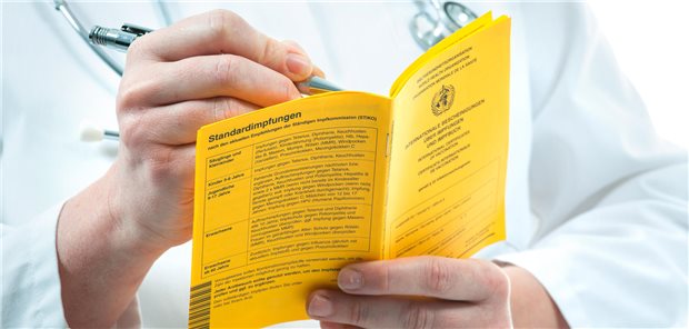 Ein Arzt fühlt die internationale Impfbescheinigung eines Patienten aus.